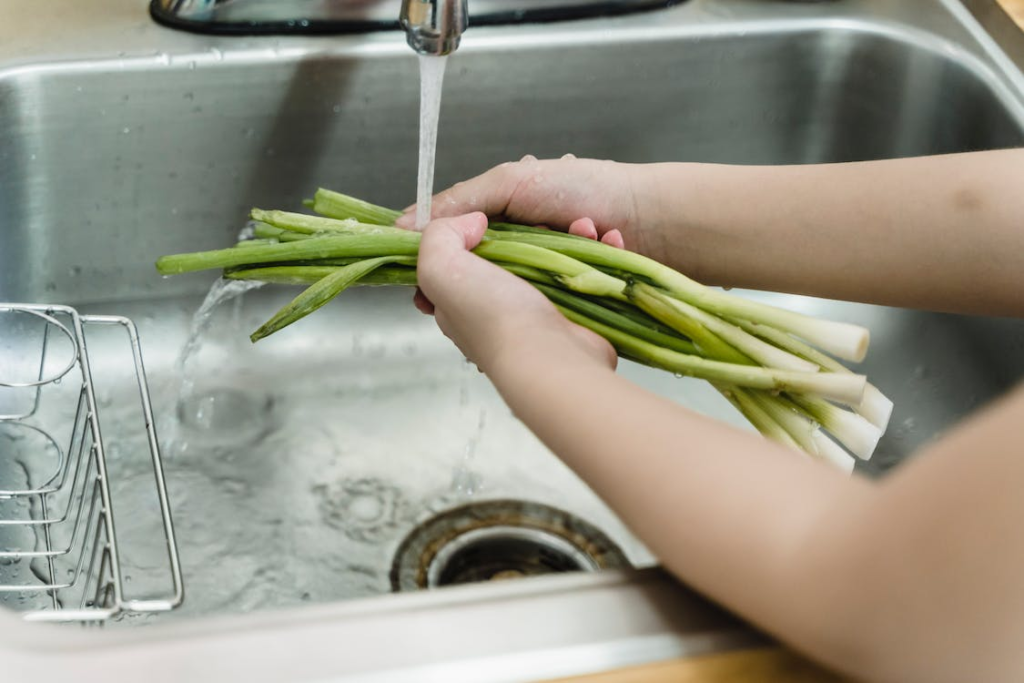 An image of a person washing vegetables over the sink