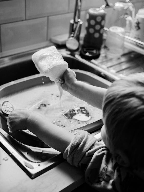 A child with a sponge dealing with a clogged kitchen sink drain