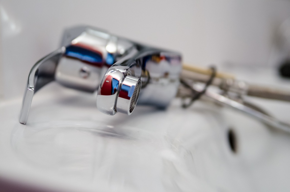 A close-up, low-angle shot of a new, shiny chrome faucet installed in a white sink, with the back of the faucet out of focus.