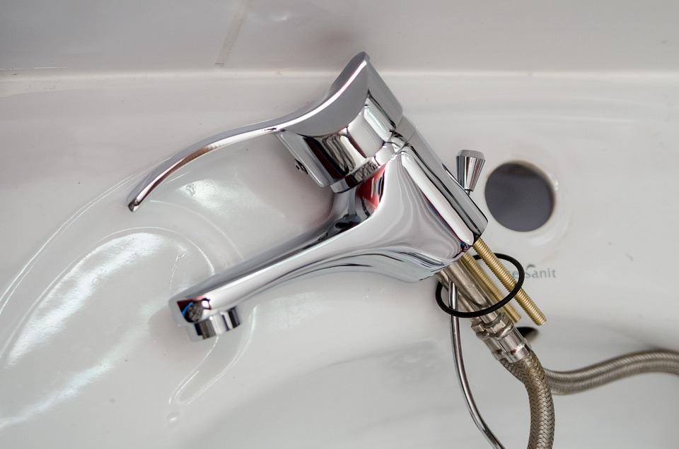 A close-up of a new chrome faucet installed in a white sink, with the water supply lines visible beneath.