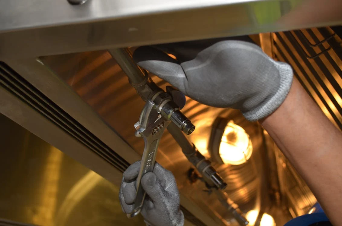 A person wearing gloves is tightening a metal pipe connection with a wrench.