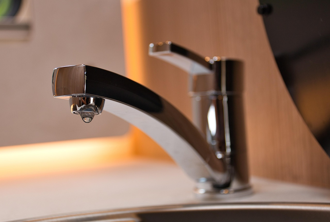 : A close-up of a modern chrome faucet with a water droplet hanging from the spout.
