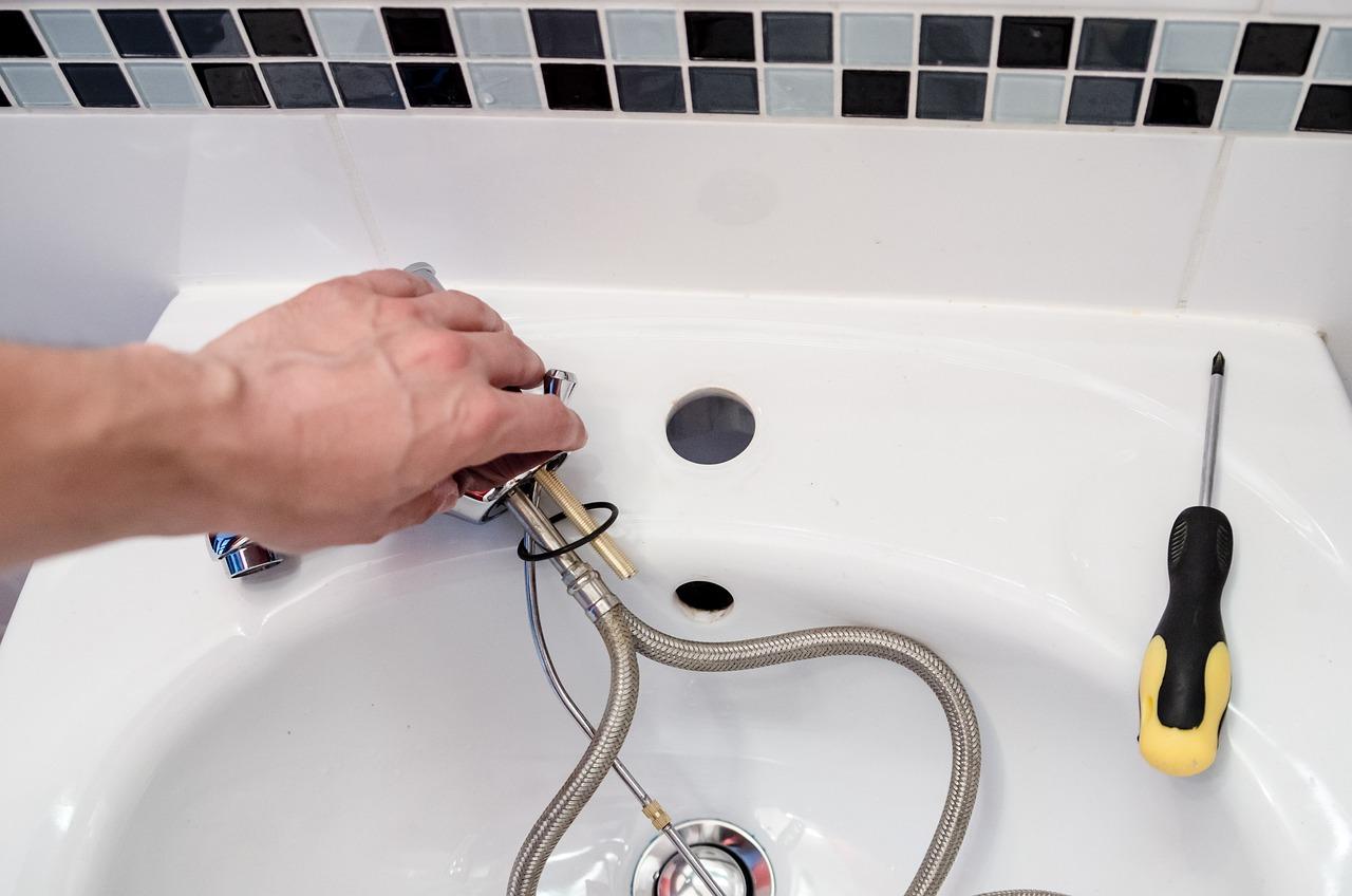 Person installing or replacing a faucet on a bathroom sink, with flexible hoses and a screwdriver visible.