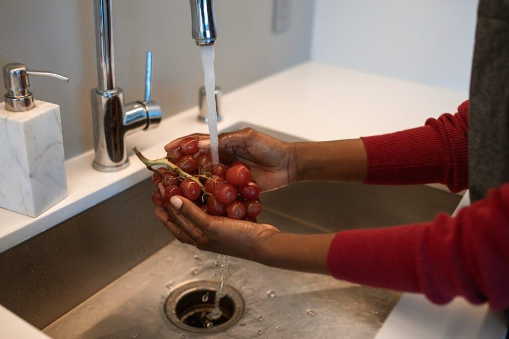 A person washing a bunch of red grapes under a kitchen faucet.