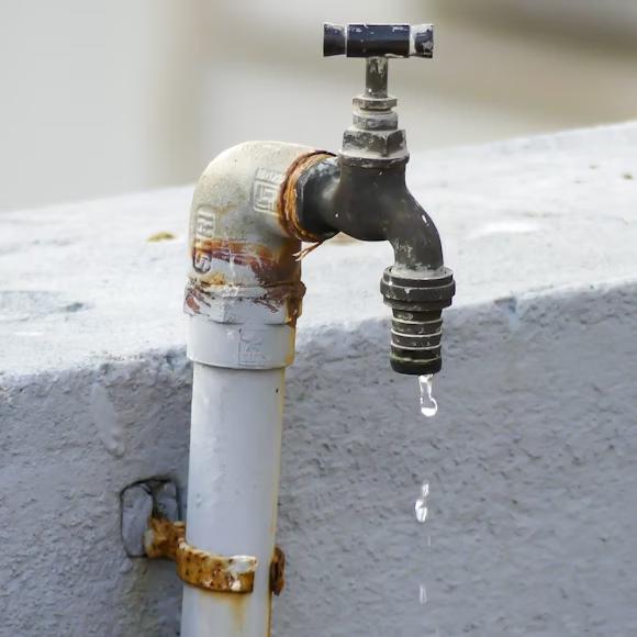 A close-up of an old, rusty outdoor water tap dripping water.