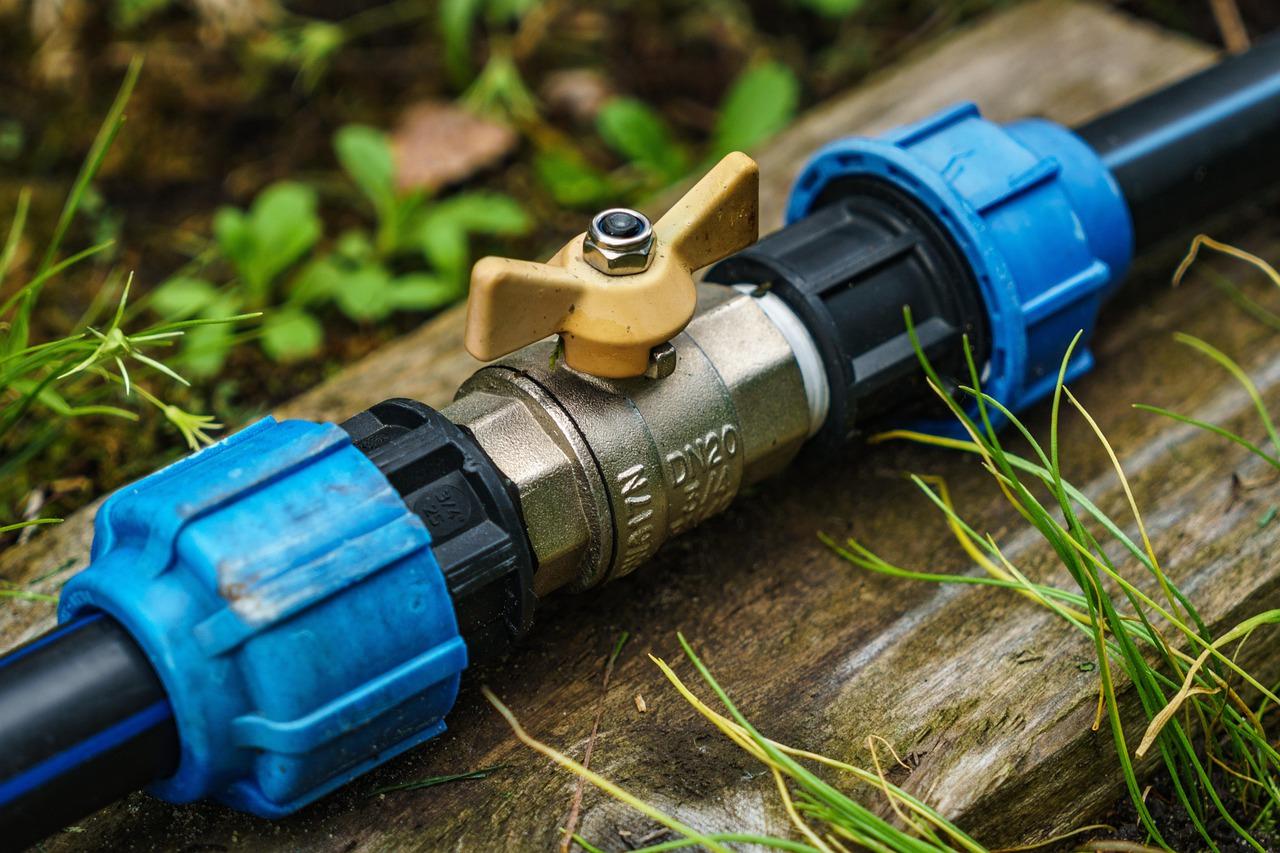 A close-up of a garden irrigation valve system with a brass shut-off valve connected to plastic tubing and compression fittings.
