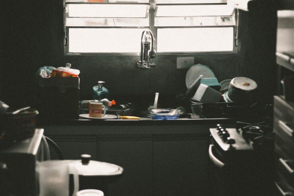 A cluttered kitchen sink area with dirty dishes, utensils, and cleaning supplies scattered around.