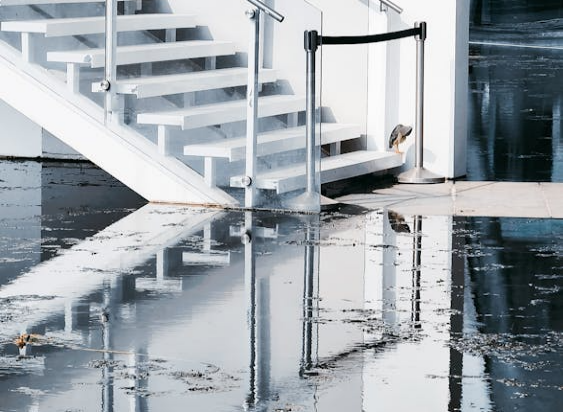 The image depicts a staircase with a reflective surface, possibly from water or a glossy floor, and a barrier in front of the stairs.