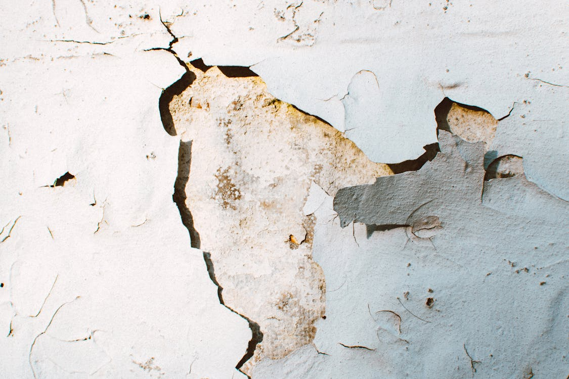 The image shows a close-up of a wall with peeling and cracked paint revealing a rough, weathered surface underneath.