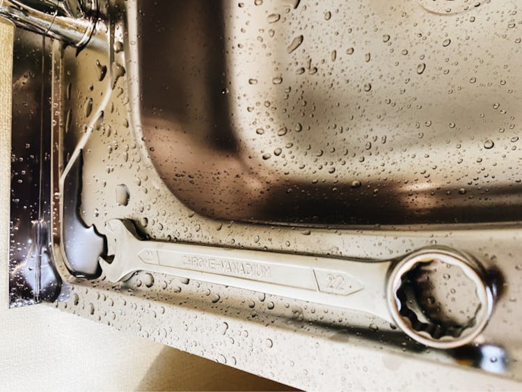 The image shows a large metal wrench resting on a stainless steel surface with water droplets.