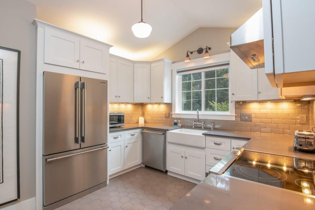 : This image shows a bright, modern kitchen with white cabinetry, stainless steel appliances, a farmhouse sink, and warm under-cabinet lighting.