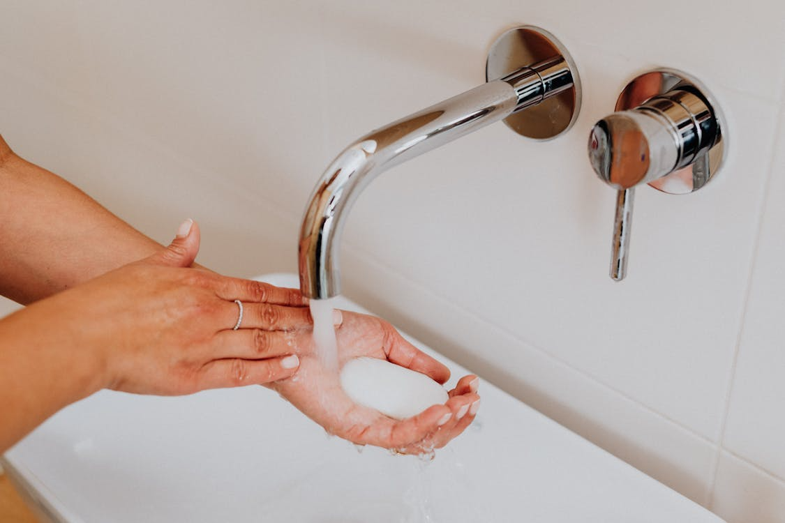 The image shows a person washing their hands under a modern faucet with water flowing into their palm.