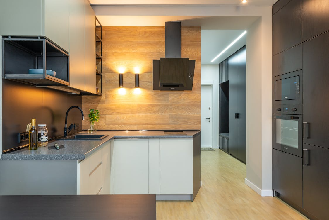 The image shows a modern kitchen with a sleek, minimalist design, featuring light-colored cabinets, dark countertops, and a stylish range hood.