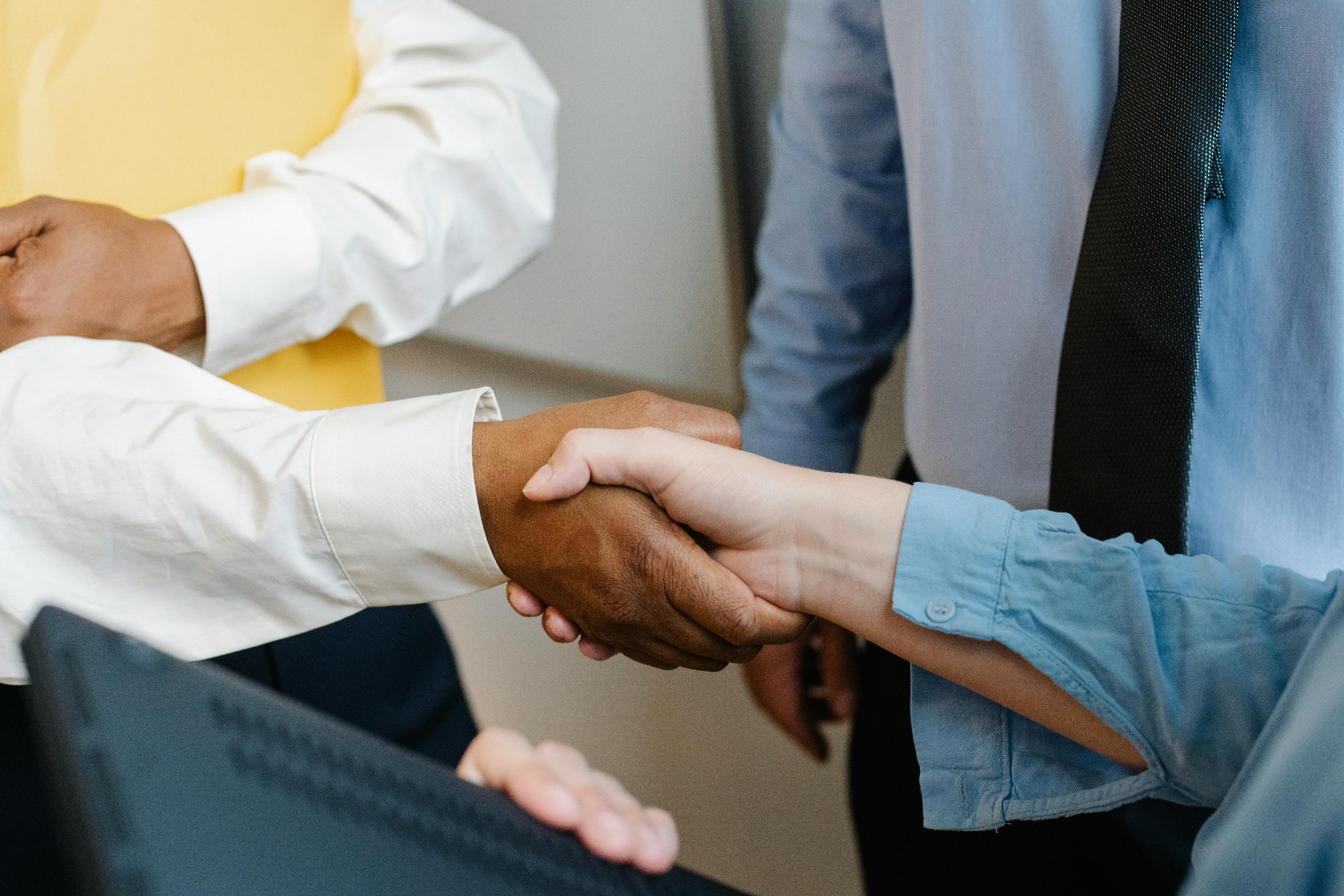  The image shows a close-up of a handshake between two people in a professional setting.