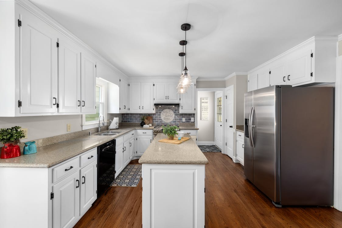 A modern kitchen with white cabinetry, stainless steel appliances, a central island, and wooden flooring.