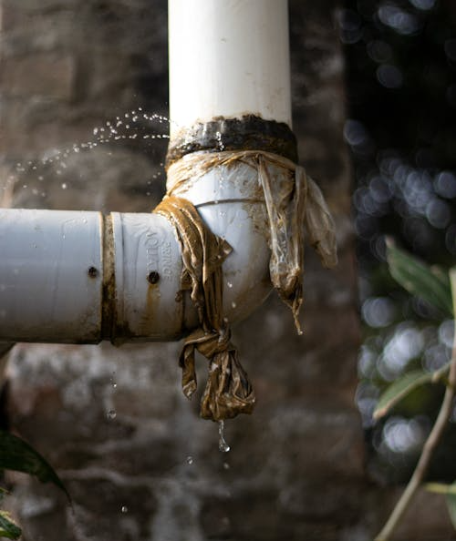 The image shows a leaking PVC pipe secured with a cloth, dripping water.