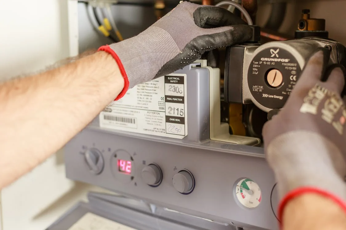 The image shows a person wearing gloves while working on a pump or heating system, adjusting the settings.