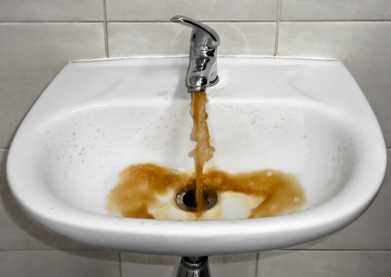 A sink faucet is pouring out dirty brown water that swirls around the drain.