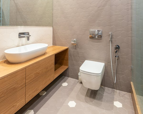 The image shows a modern, minimalist bathroom with hexagonal tiles, a wooden vanity, and a contemporary toilet.