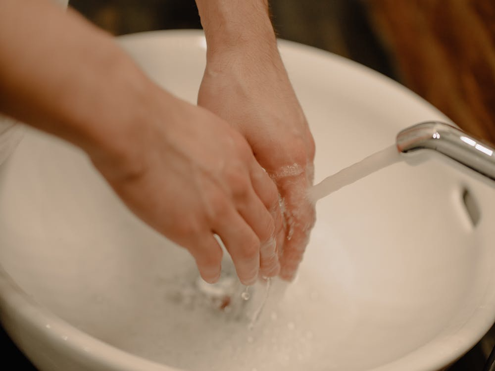 The image shows a person washing their hands under running water from a faucet.
