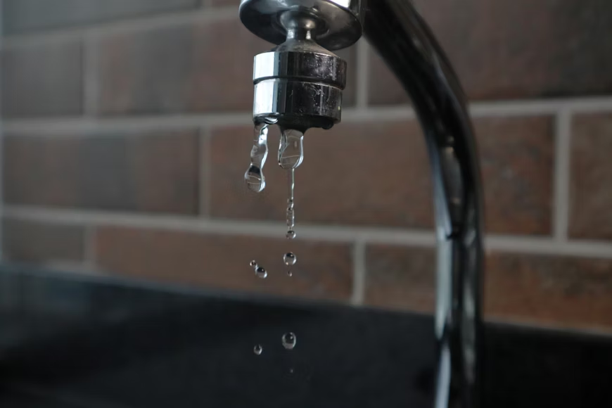 The image shows a close-up of a kitchen faucet with water droplets dripping from it