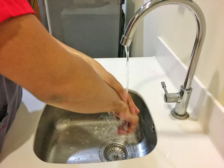 A person washing their hands under running water in a stainless-steel sink.