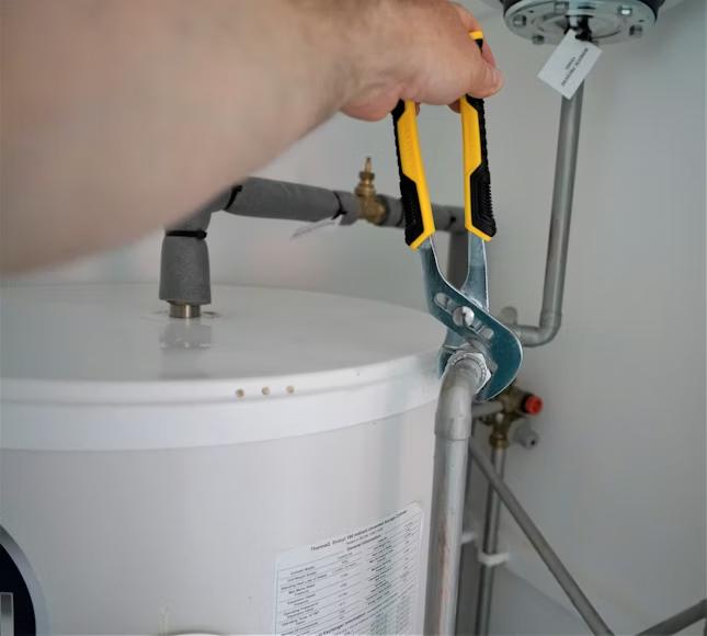 A person using pliers to adjust a pipe connection on a water heater.