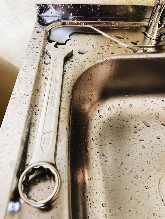 A wet metal sink speckled with water droplets, with a wrench resting along its edge.