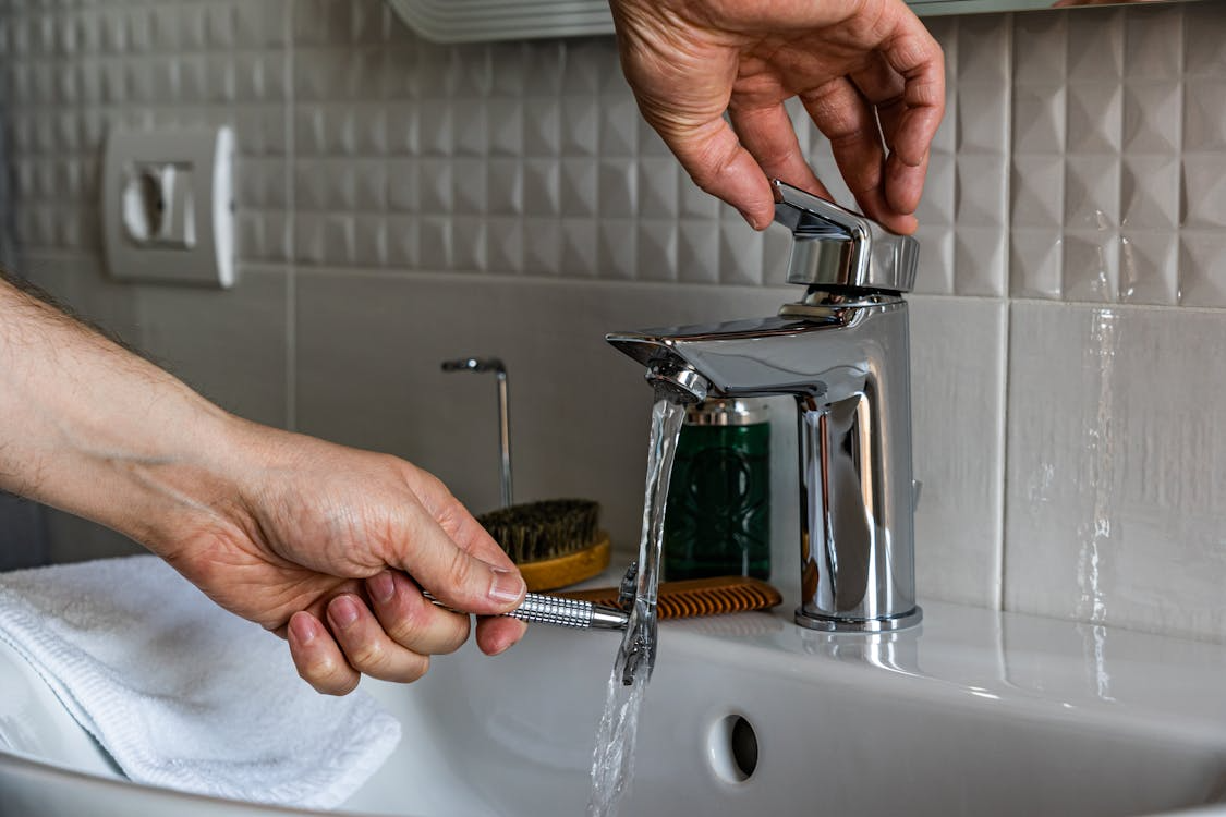 Hands adjusting a modern bathroom faucet as water flows into a white sink.
