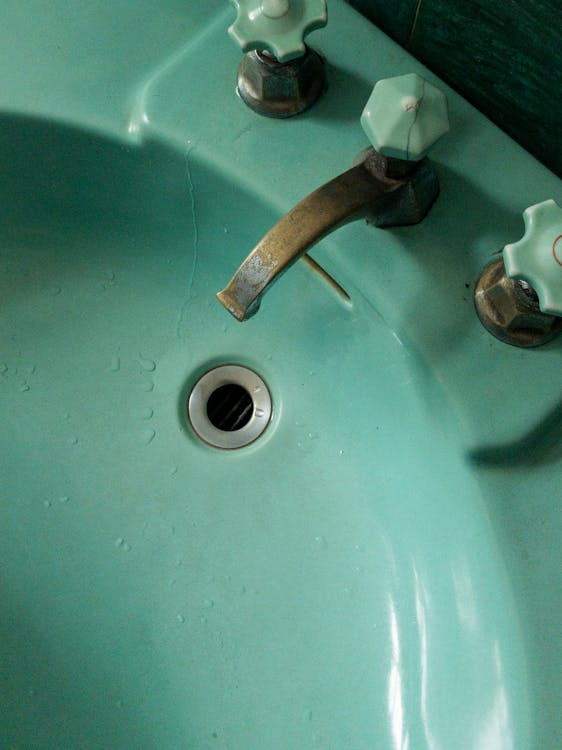 A vintage green sink with worn metal faucets and water droplets around the drain.