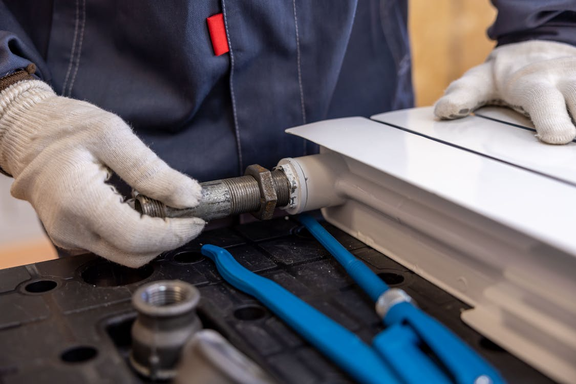 A gloved worker is tightening a metal pipe connection with tools on a workbench.
