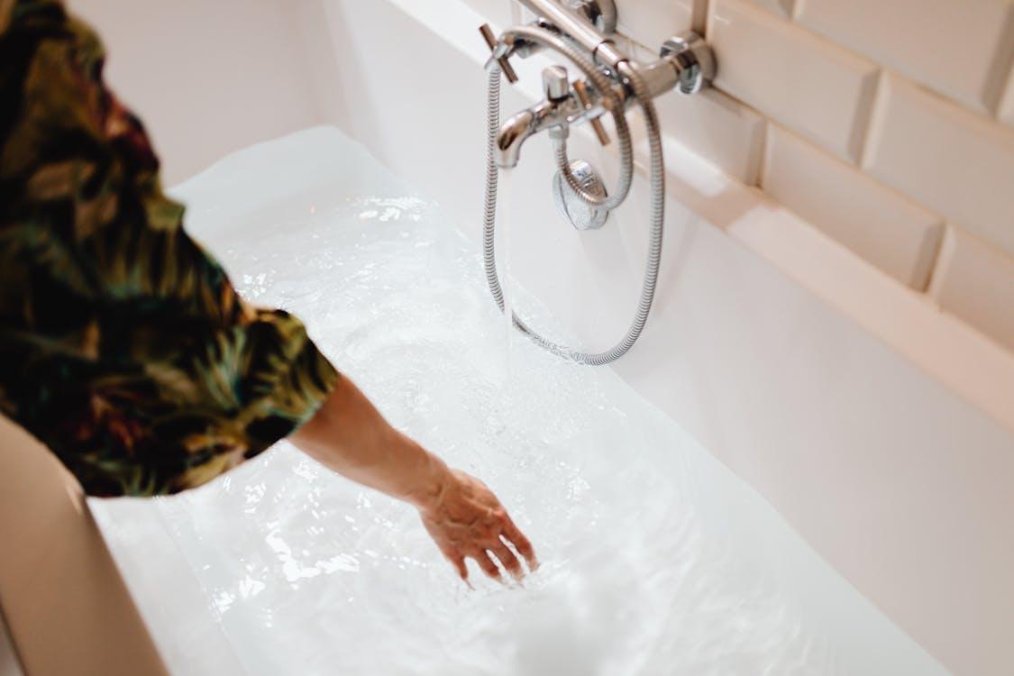  This photo shows a person touching water in a bathtub.