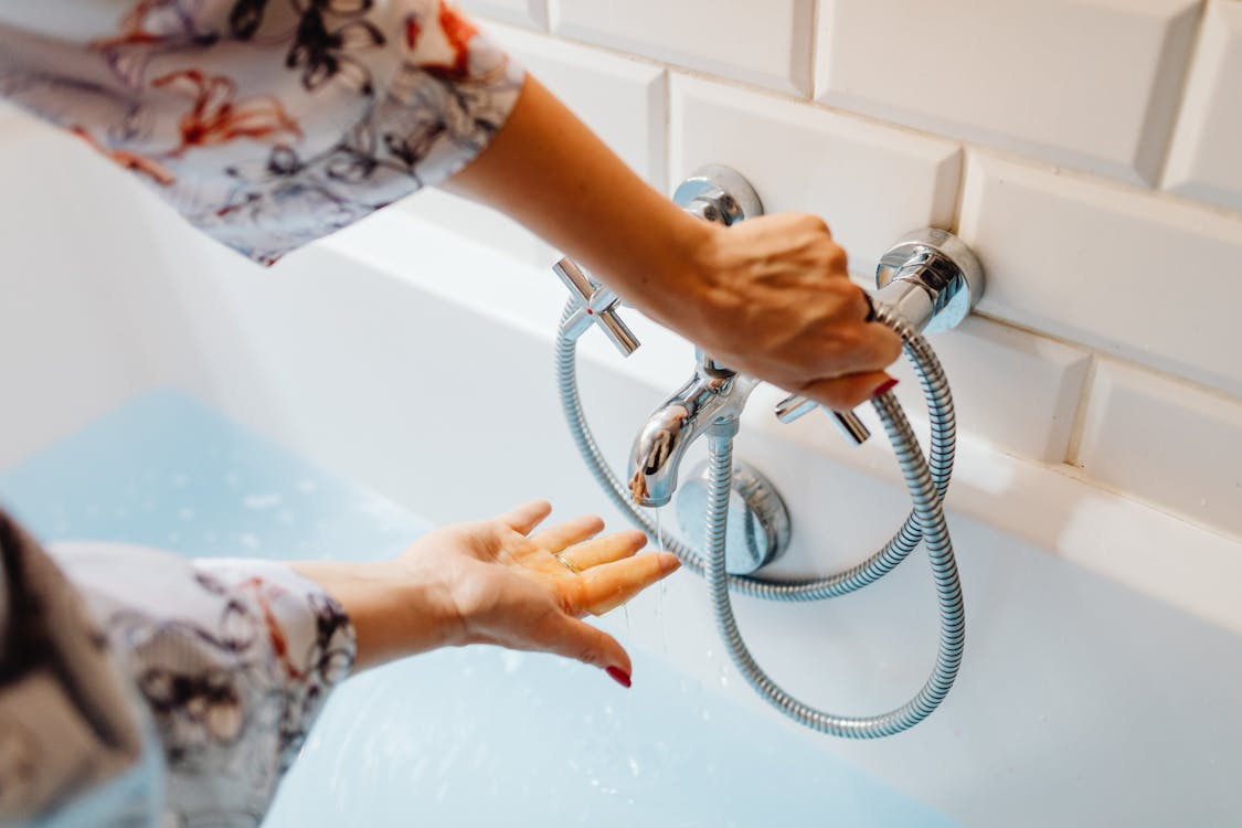 A close-up of hands adjusting the water temperature of a bath faucet.