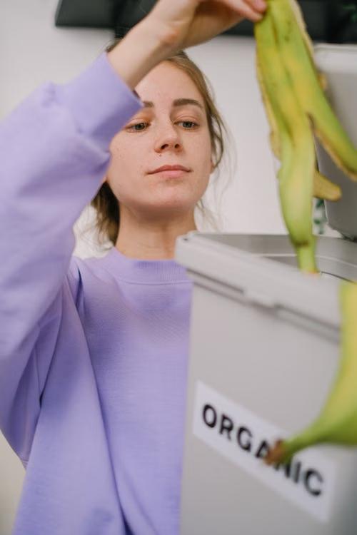 Woman putting a banana peel into an organic waste bin in a kitchen.